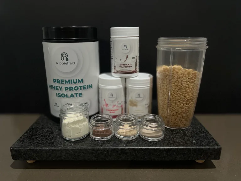 Ripple Effect Performance protein product display featuring Premium Whey Protein Isolate tub, Chocolate Temptation, Strawberry Bliss, and Vanilla Sensation flavour tubs, small sample jars of protein powders, and a blender cup filled with Rice Krispies cereal on a black countertop.